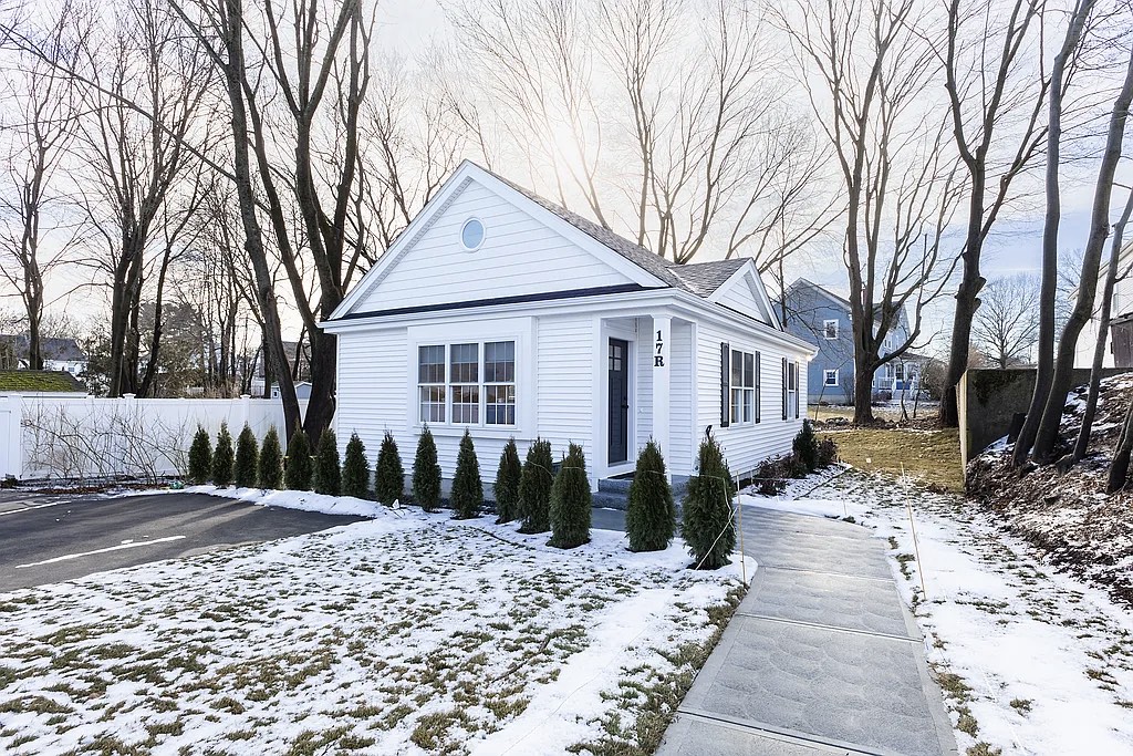 Front elevation of the completed 756 sf ADU at 17R Harding Rd, Norwood &mdash; white clapboard with a gable roof, round attic window, and covered entry
